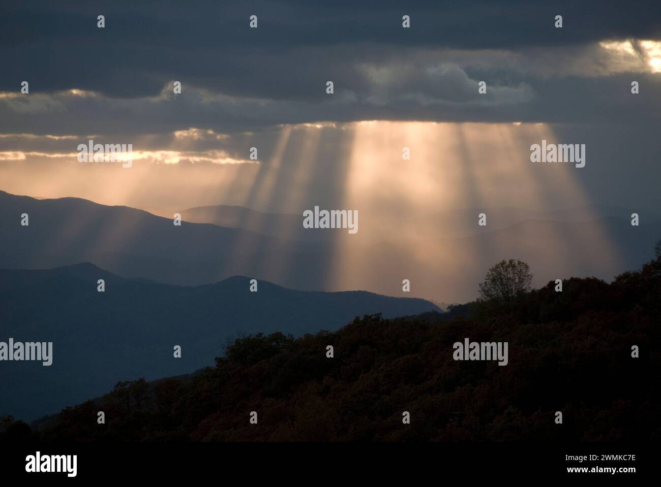 Sunlight streams through breaks in the grey clouds over the Blue Ridge Mountains at twilight; North Carolina, United States of America Stock Photo