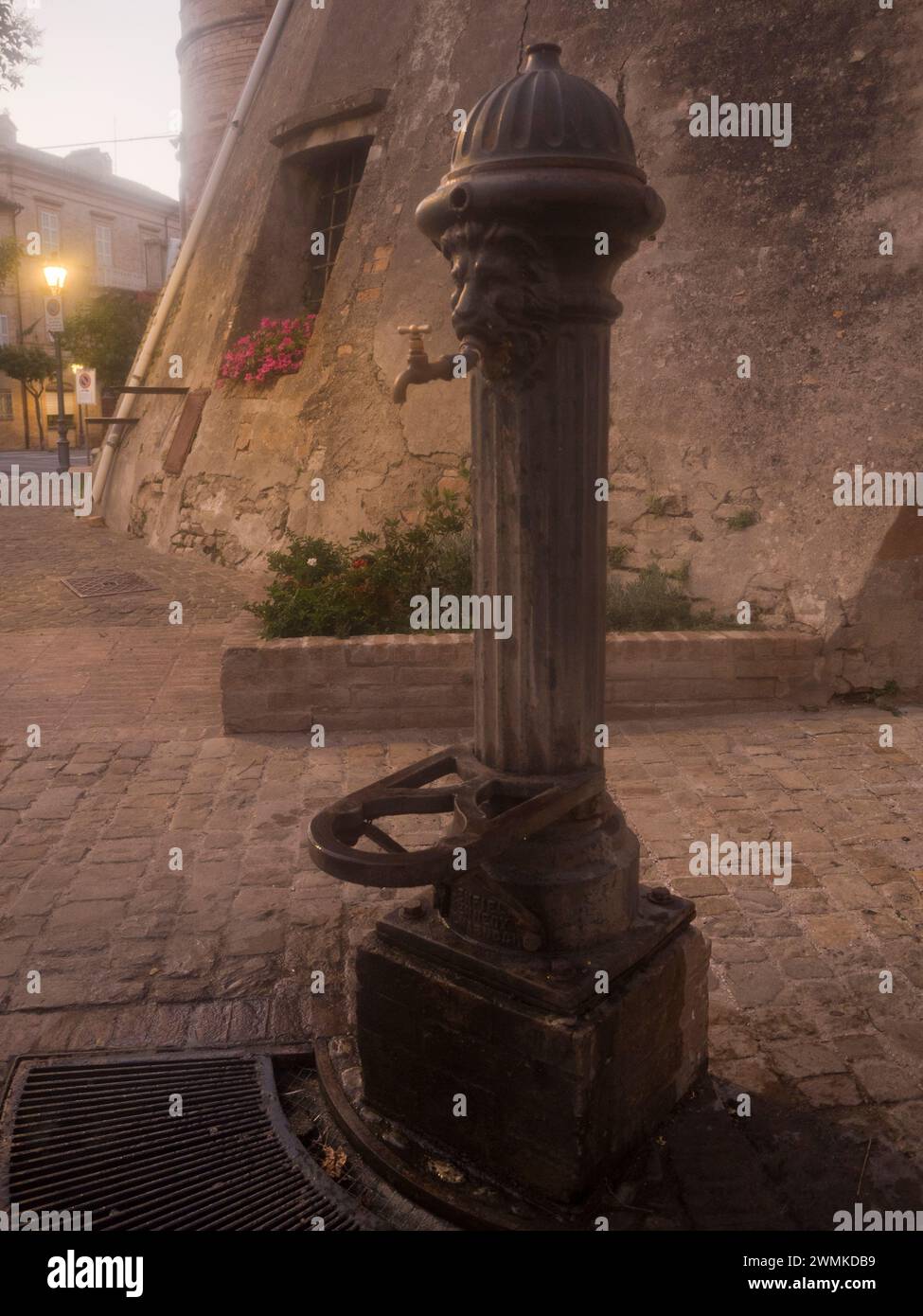 Cast iron public water fountain with the head of a lion at dusk; Grottazzolina, Marche region, Italy Stock Photo