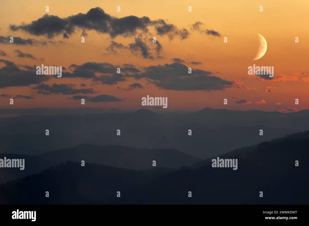 Crescent moon glows in an illuminated sky at sunset over the silhouetted Blue Ridge mountains; Fairview, North Carolina, United States of America Stock Photo