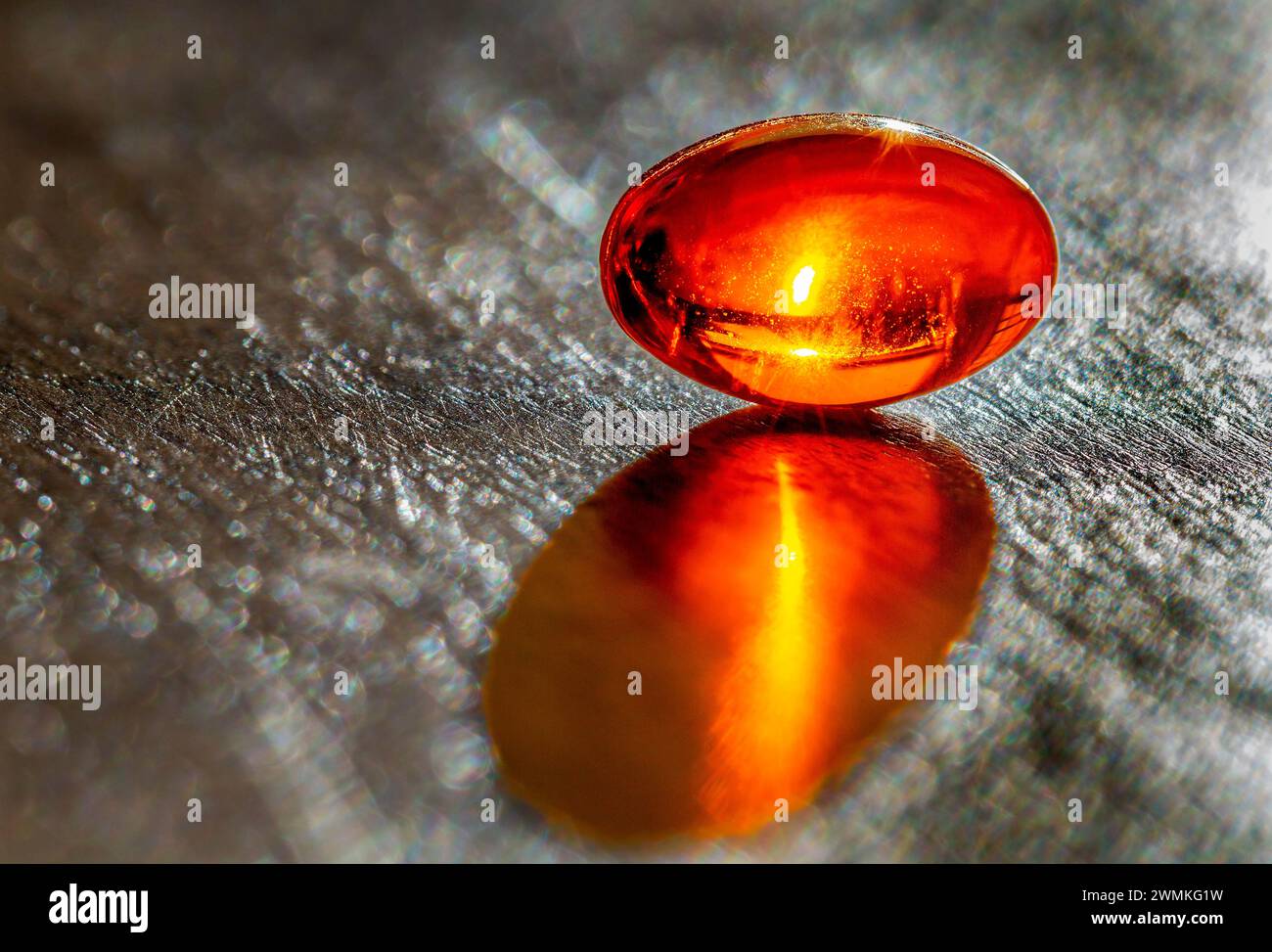 Close up of a glowing gel capsule with a sun glow inside on a grey slate background; Studio Shot Stock Photo