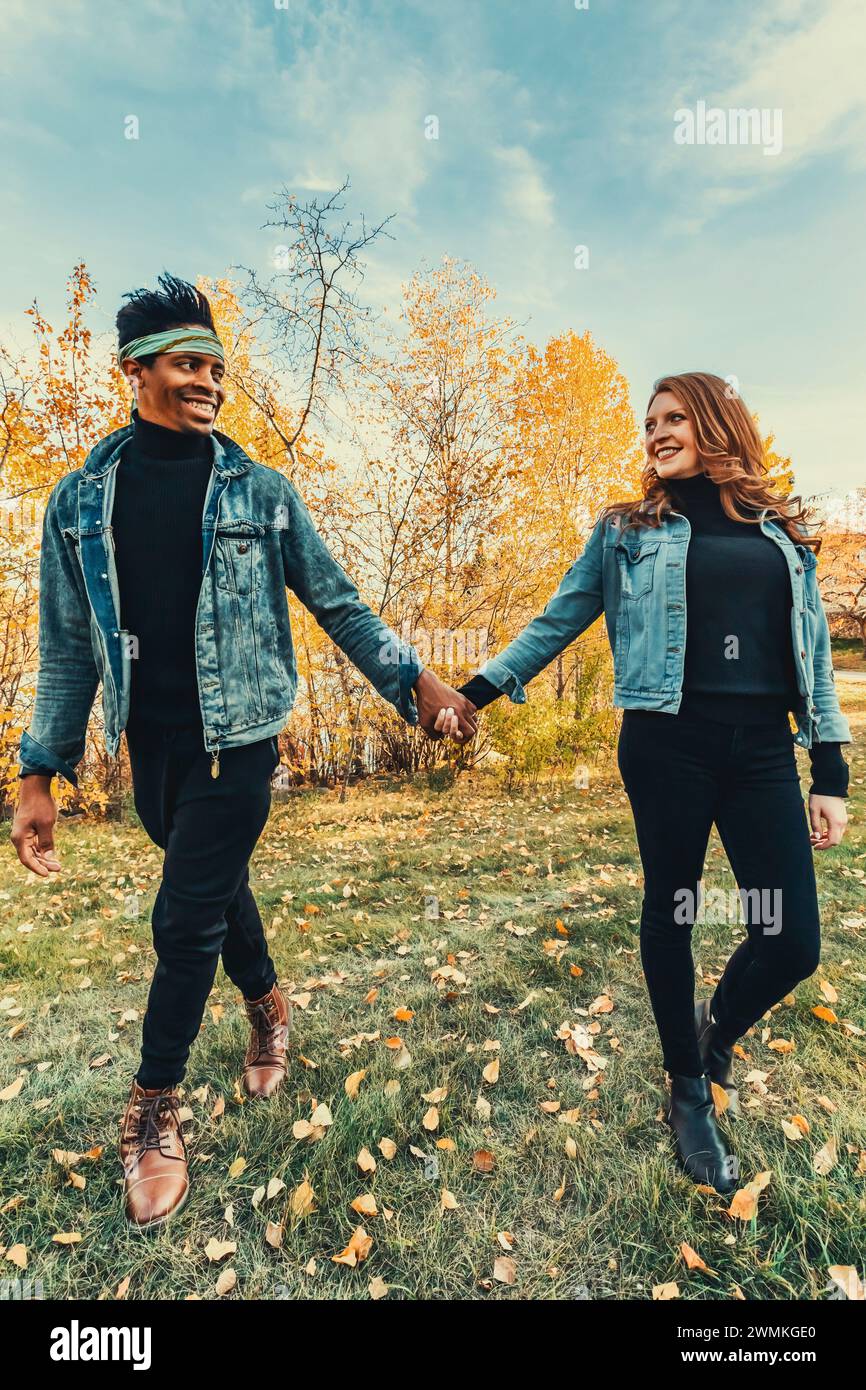 Mixed race married couple smiling at each other, walking in a city park during a fall family outing, spending quality time together Stock Photo