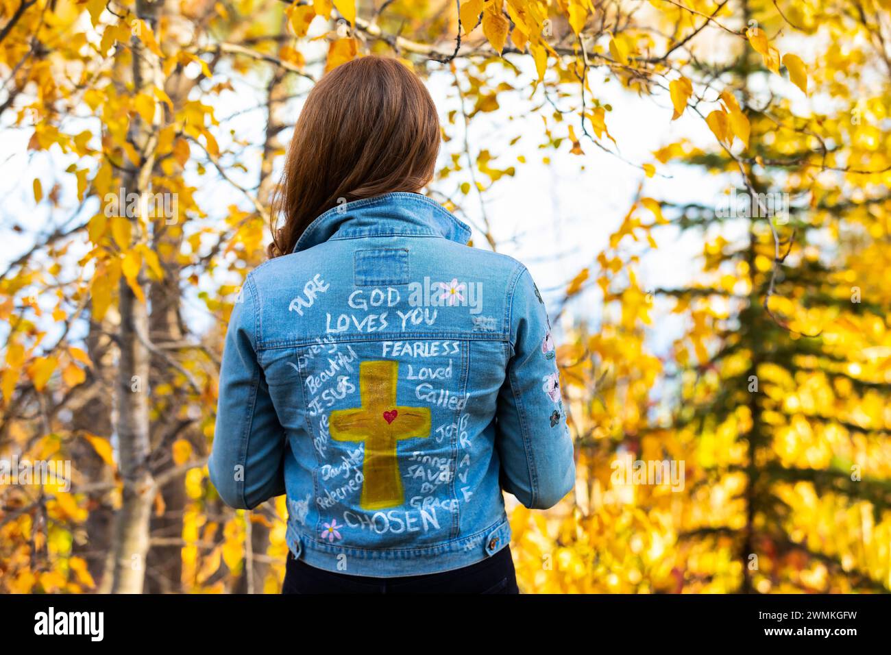 Close-up view from behind of a woman wearing a jean jacket with hand-written Christian references during a fall outing in a city park Stock Photo