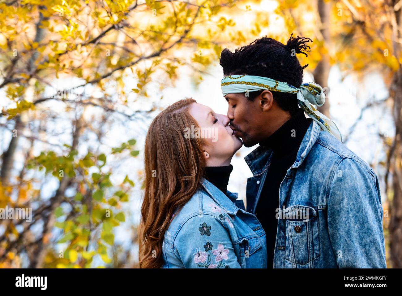 Close-up of a mixed race married couple kissing each other during a fall family outing in a city park, spending quality time together Stock Photo