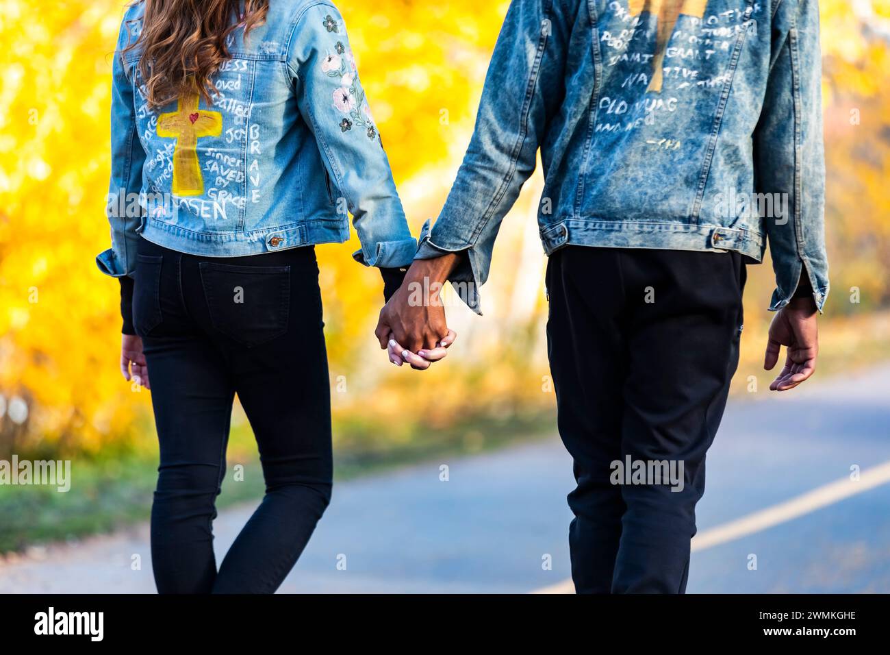 View from behind of a mixed race couple holding hands and spending quality time together during a fall family outing in a city park Stock Photo