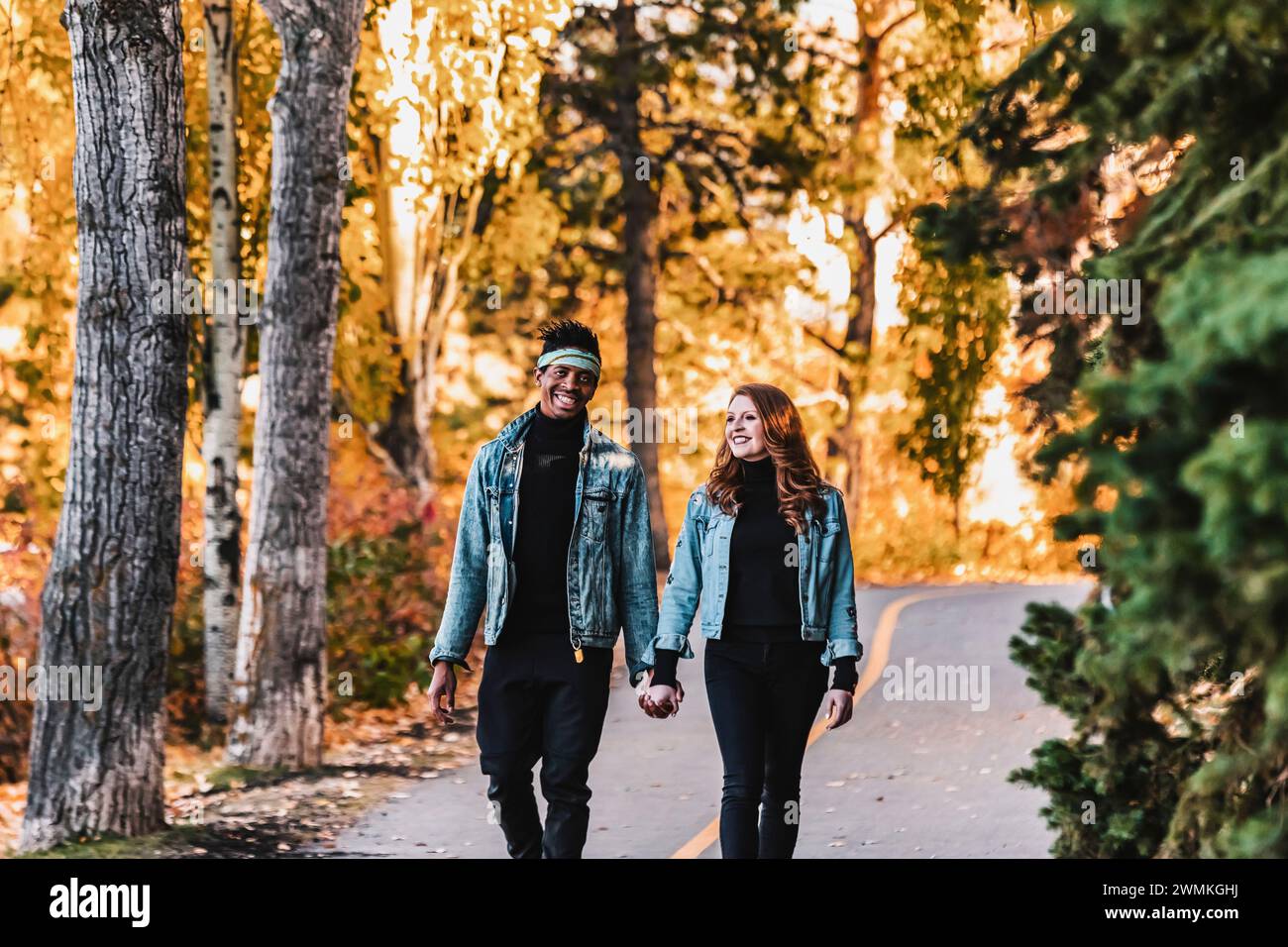 A mixed race married couple walking down a road in a city park during a fall family outing, holding hands, spending quality time together Stock Photo