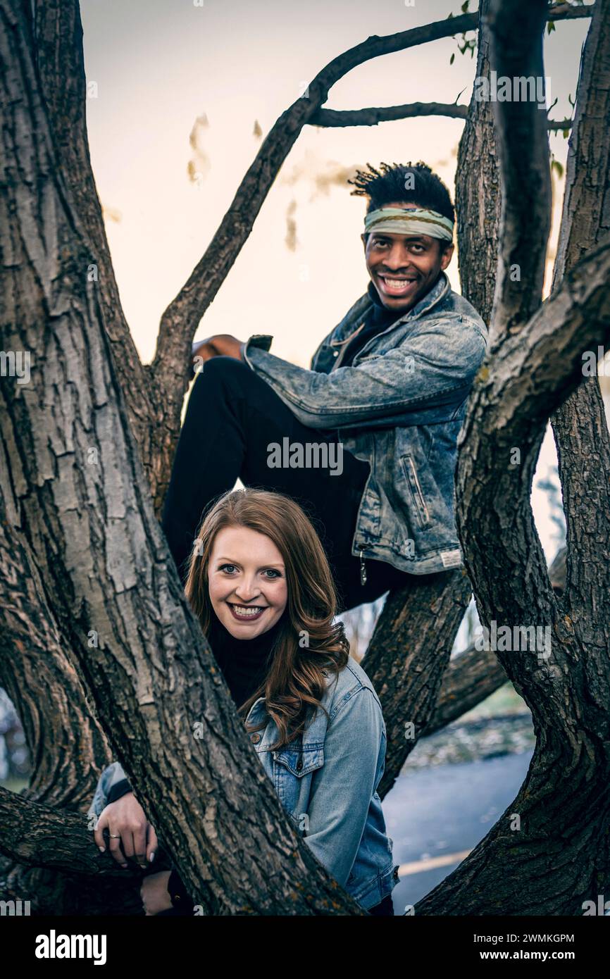 Close-up portrait of a mixed race couple smiling and looking at the camera through tree branches, spending quality time together during a fall fami... Stock Photo