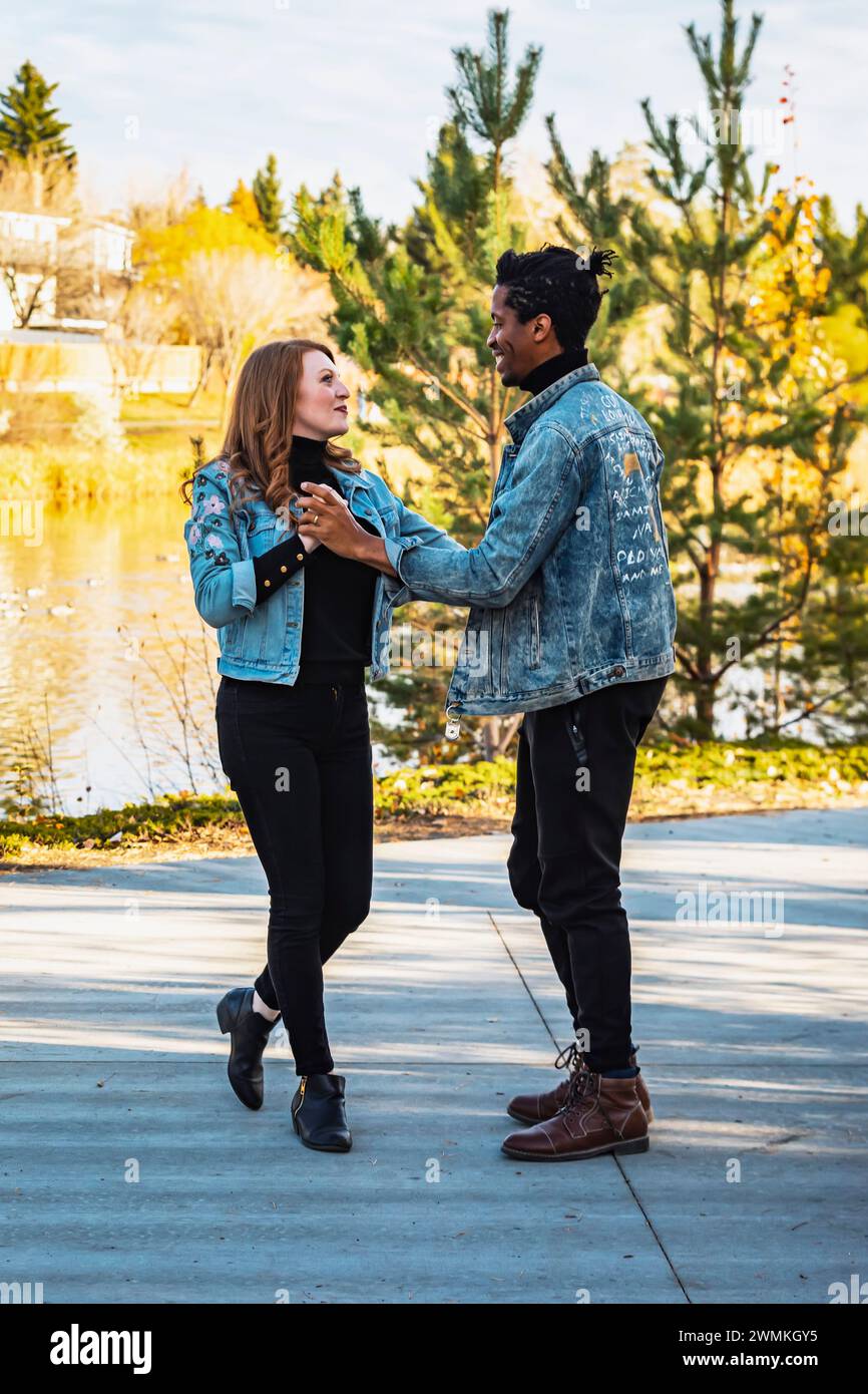 A mixed race couple dancing and having fun while spending quality time together during a fall family outing in a city park; Edmonton, Alberta, Canada Stock Photo