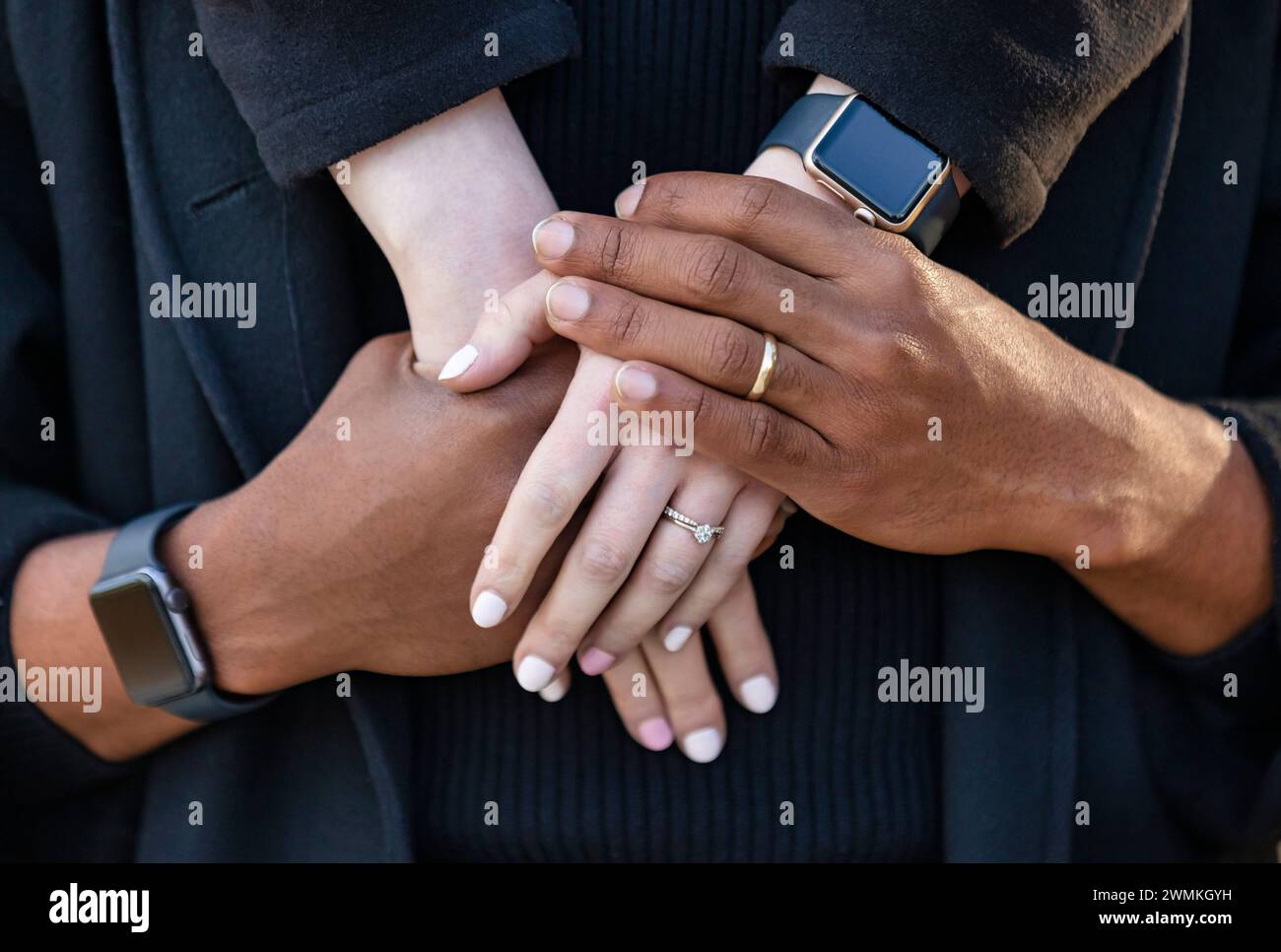 Close-up of the interlocked hands of a mixed race couple, spending quality time together during a fall family outing in a city park Stock Photo