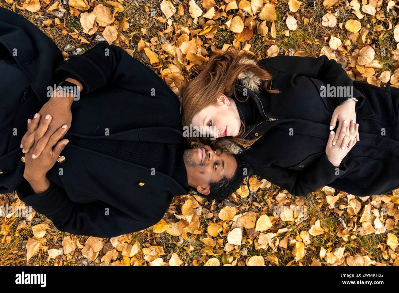 A mixed race couple lying on the ground in the fall leaves, looking at each other face to face, while spending quality time together during a fall ... Stock Photo
