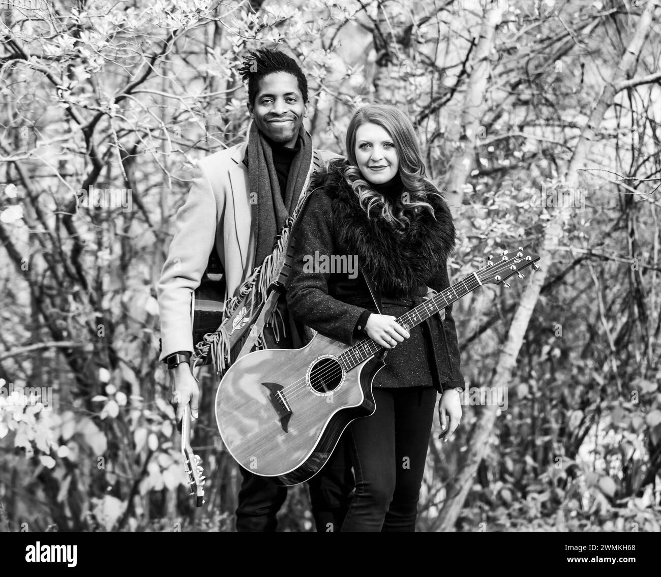 Portrait of a mixed race married couple holding acoustic guitars and smiling at the camera while spending quality time together during a fall famil... Stock Photo