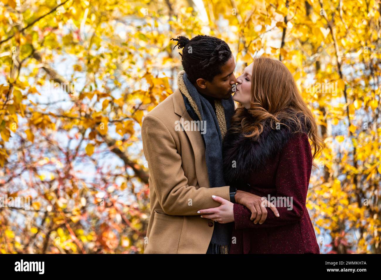 A mixed race married couple hugging and kissing each other while spending quality time together during a fall family outing in a city park Stock Photo