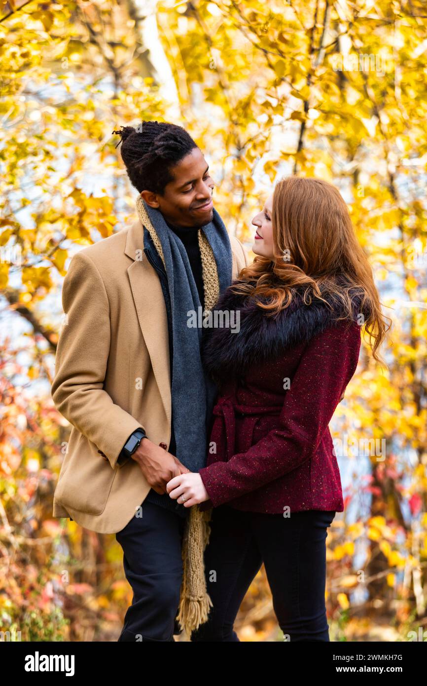 Close-up portrait of a mixed race married couple smiling at each other and holding hands while spending quality time together during a fall family ... Stock Photo