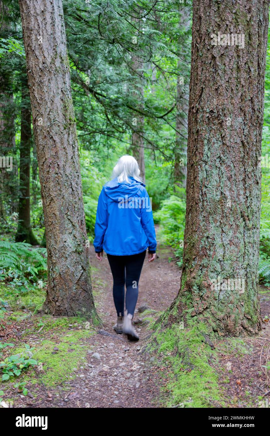 View taken from behind of a woman walking along a dirt path through Watershed Forest Trail; Delta, British Columbia, Canada Stock Photo