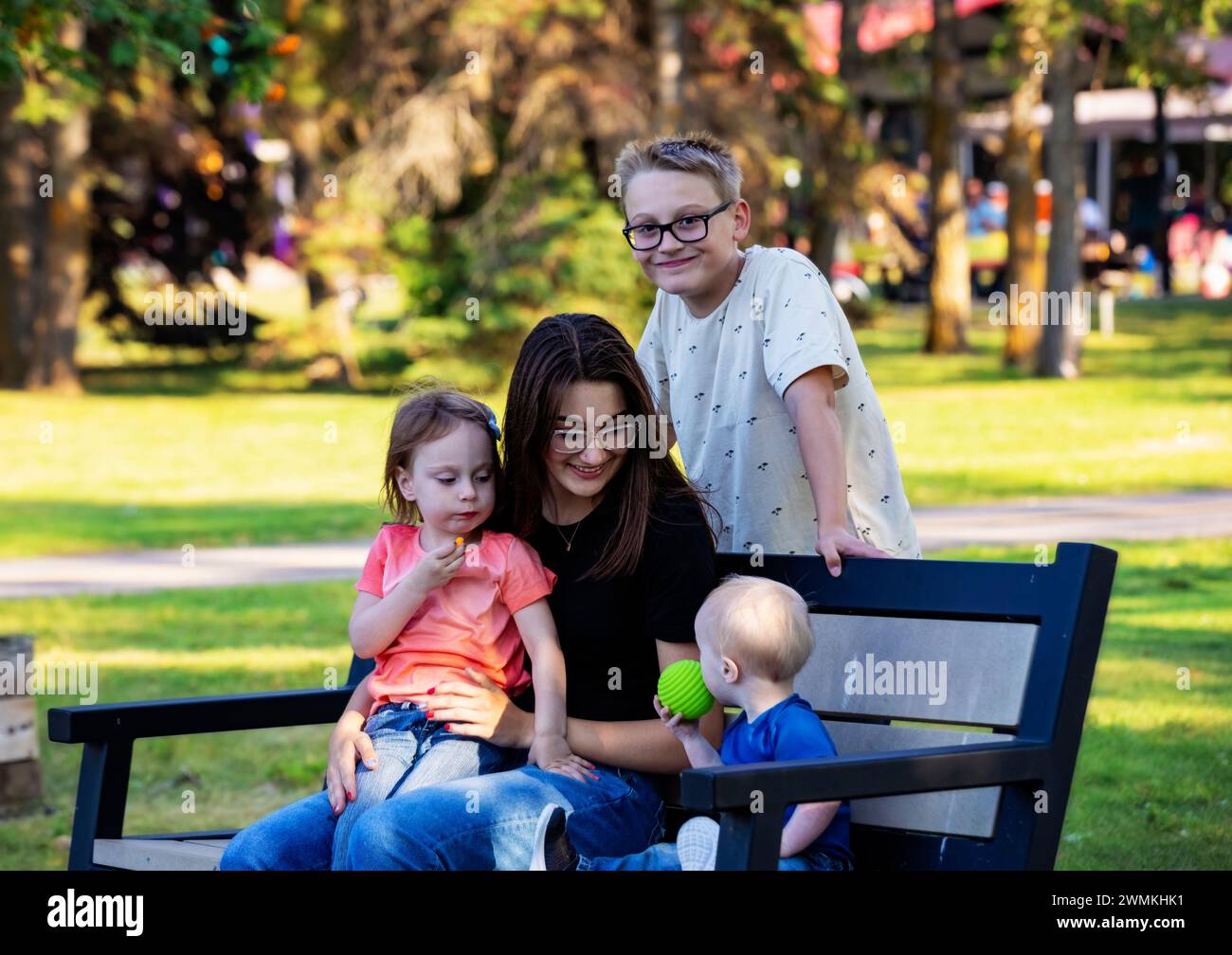 Portrait of four sibilings enjoying quality time together in a city park, during a warm fall afternoon and the youngest boy has Down Syndrome Stock Photo
