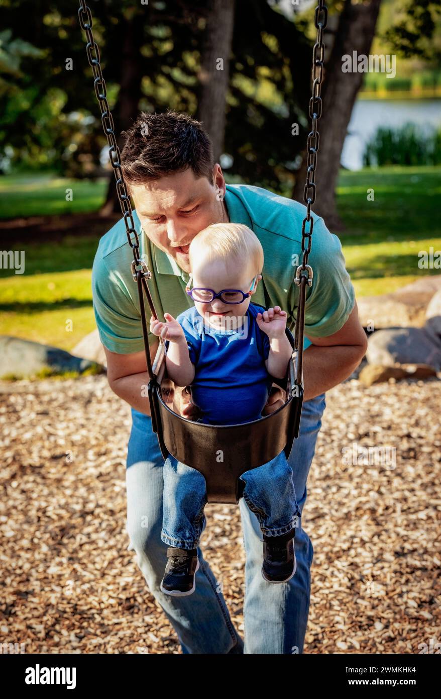 Father spending quality time with his son who has Down Syndrome, pushing him on a swing in a city park, during a warm fall afternoon Stock Photo