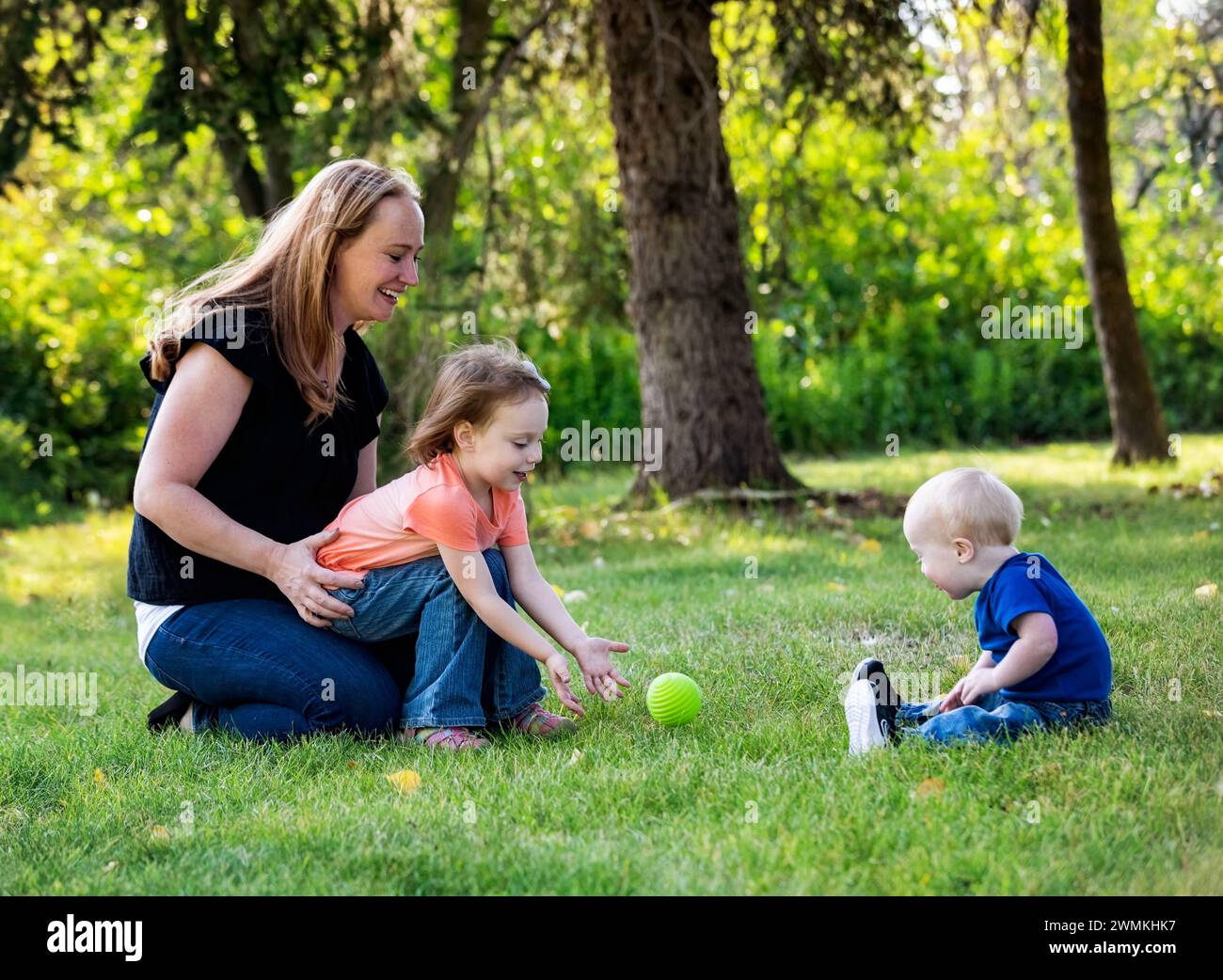 Mother throwing a ball with her daughter, and her young son who has Down Syndrome, in a city park during a warm fall afternoon; Leduc, Alberta, Canada Stock Photo