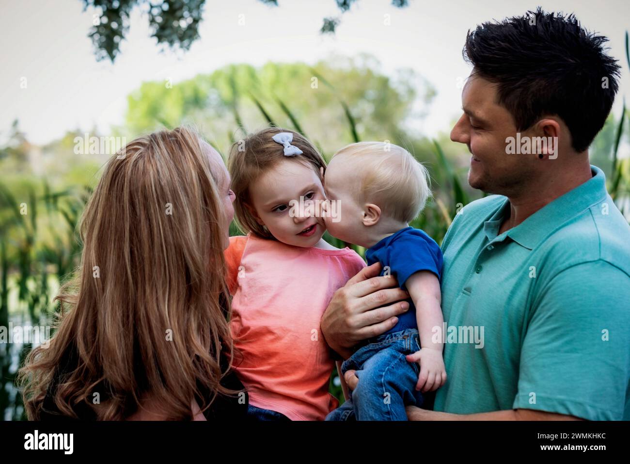 Young boy who has Down syndrome kisses his sister while the mother and father look on; Leduc, Alberta, Canada Stock Photo