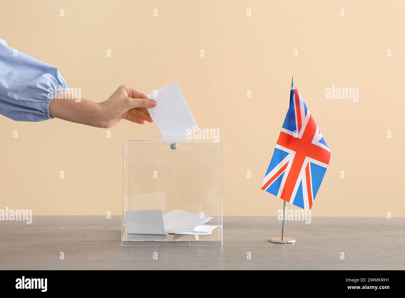 Voting young woman with UK flag near ballot box on table at polling station Stock Photo