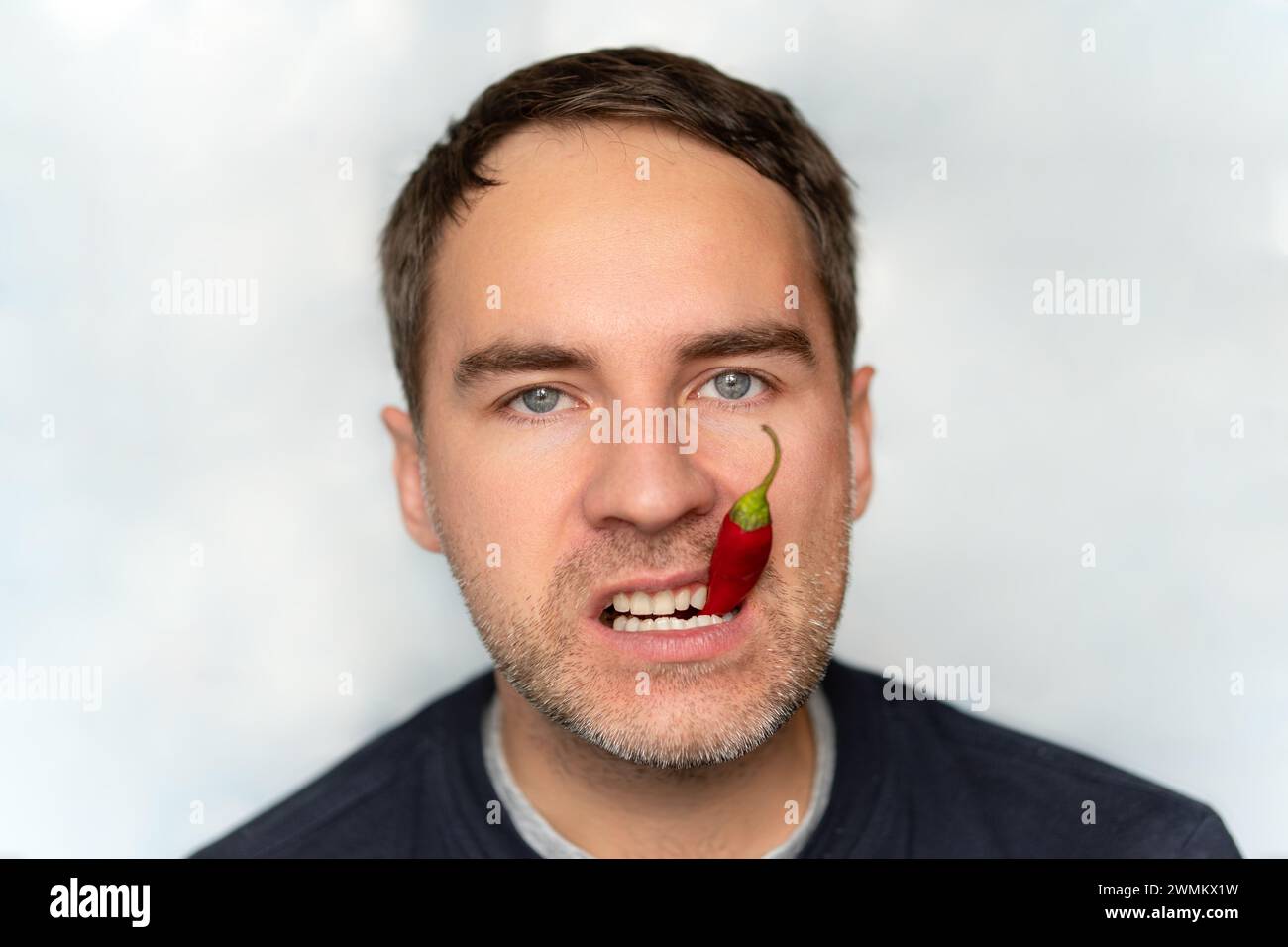 Portrait of young man eating chili pepper. red hot pepper in the mouth close-up Stock Photo