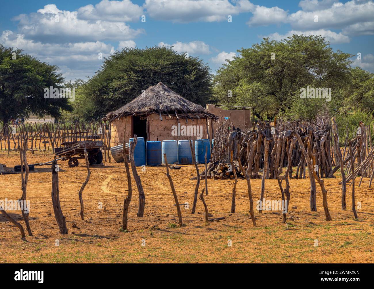 village african hut with thatched roof ,outdoors kitchen on the side , water drums and cart in the front Stock Photo
