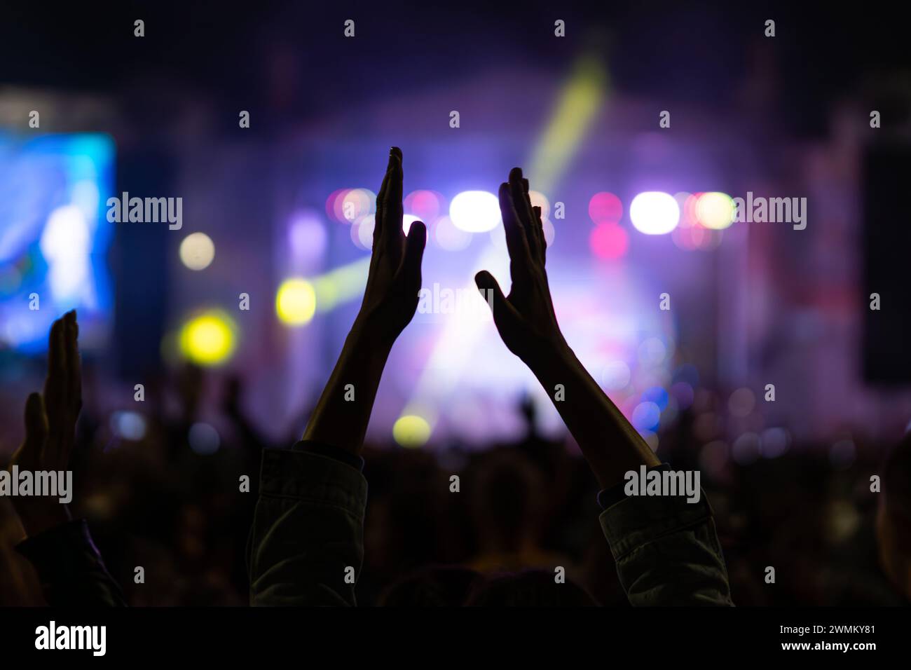 woman claps his hands at a musical concert in a crowd of people. clapping crowd at singer's concert. smoke, applause and hands in soft focus, abstract Stock Photo