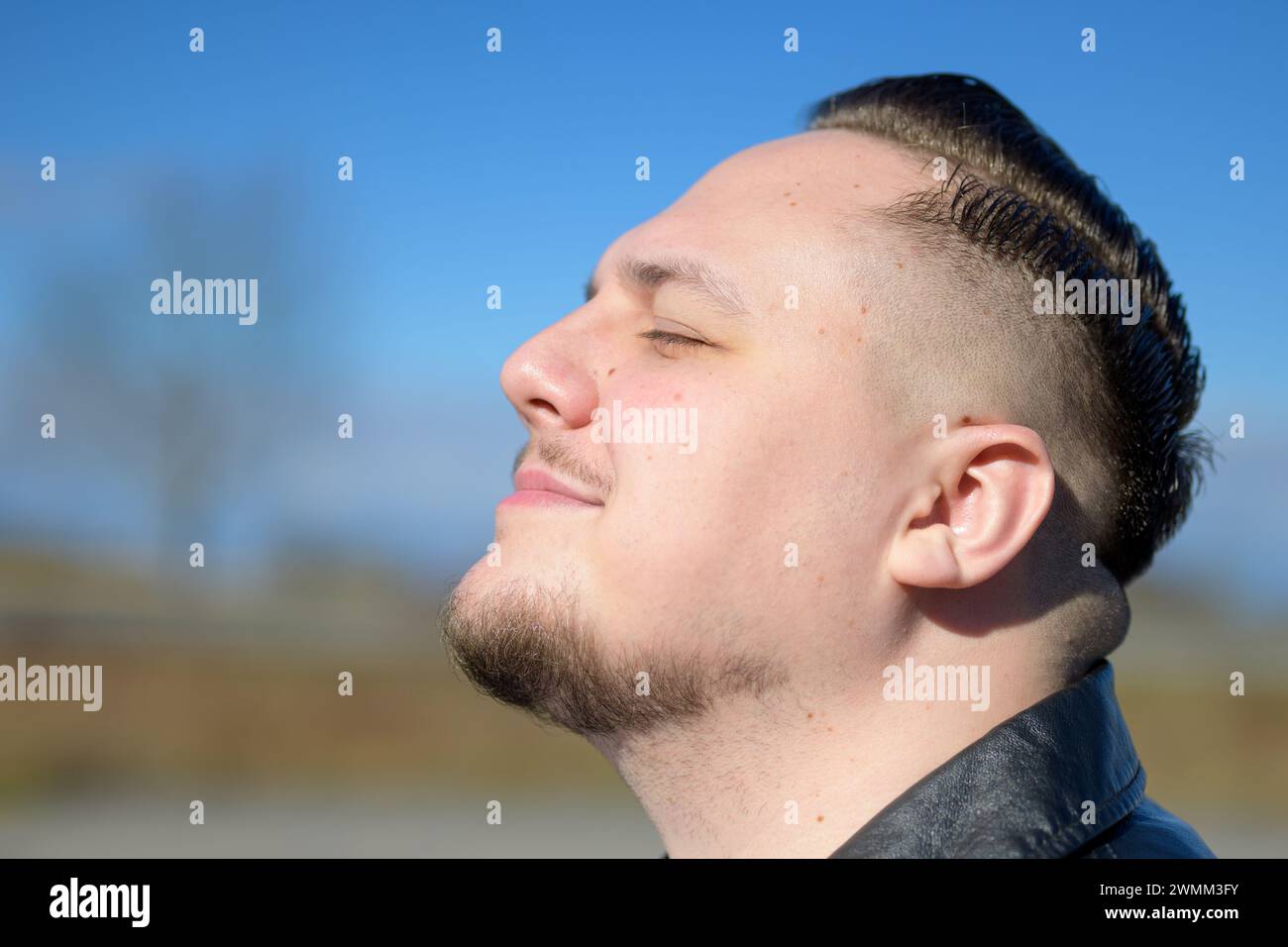 Young attractive man enjoying the sun in a park with eyes closed Stock Photo