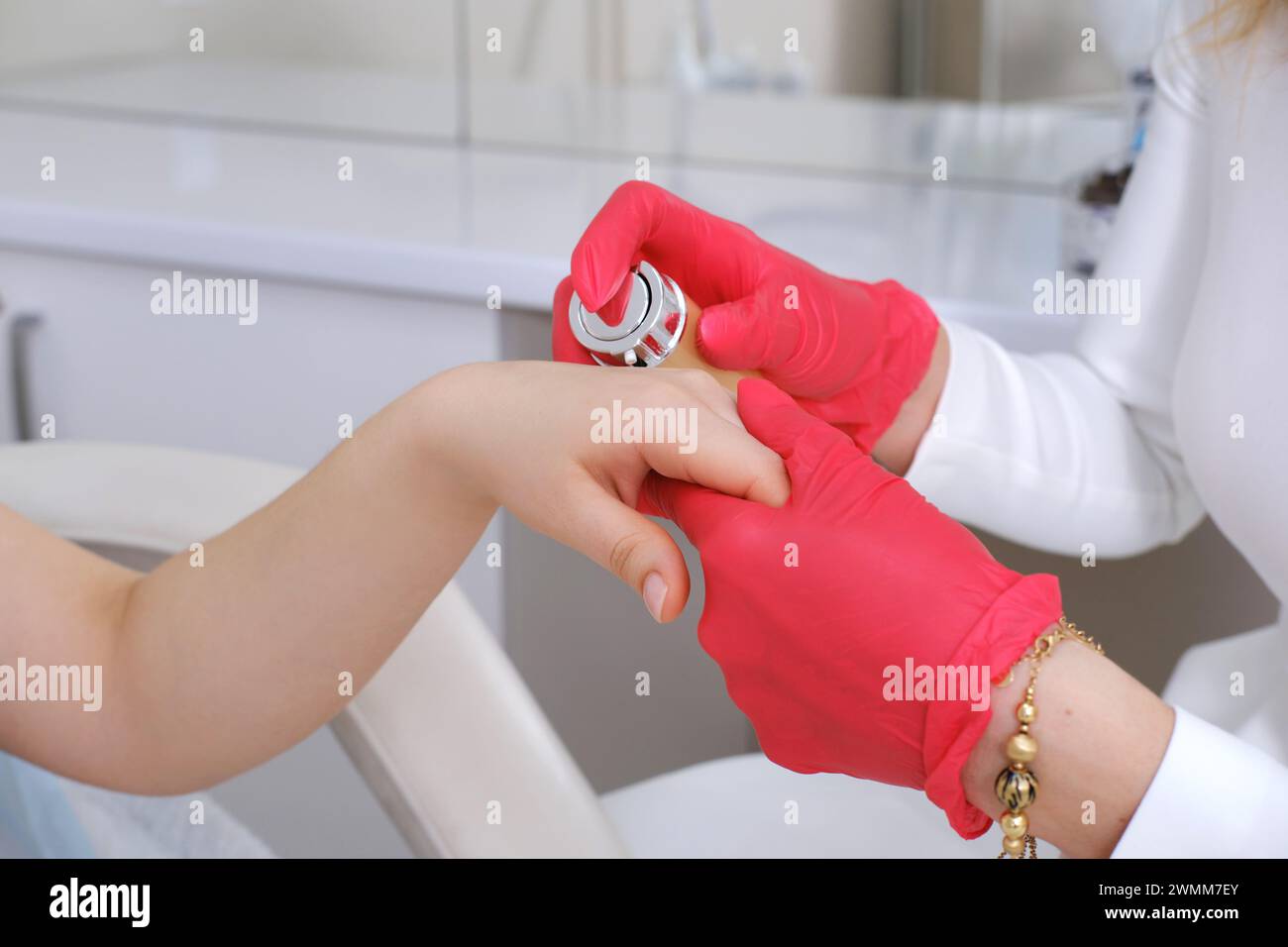 A cosmetologist in red gloves applies cream to a client's hand, with a focus on skincare treatment Stock Photo