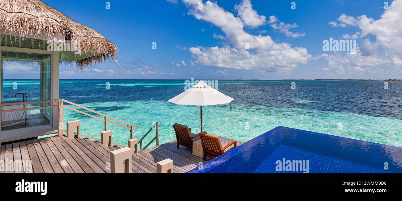 Luxury beach resort, bungalow near endless pool over beautiful blue sea. Amazing tropical island, summer vacation concept. Couple chairs with umbrella Stock Photo