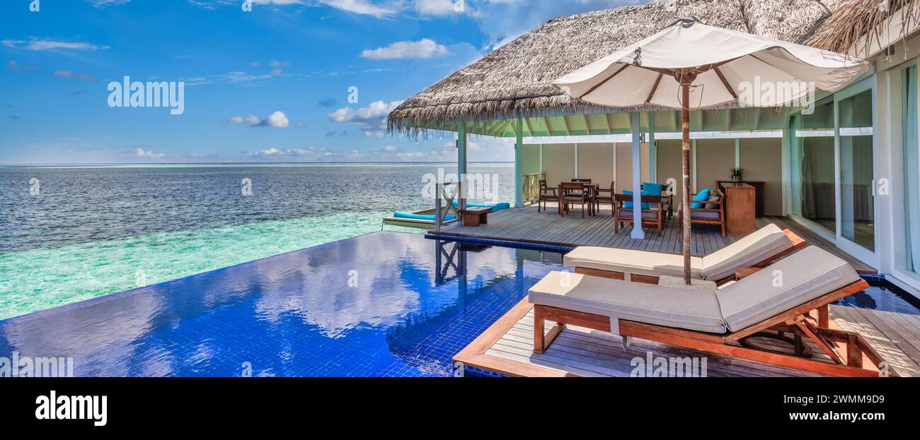 Luxury beach resort, bungalow near endless pool over beautiful blue sea. Amazing tropical island, summer vacation concept. Couple chairs with umbrella Stock Photo
