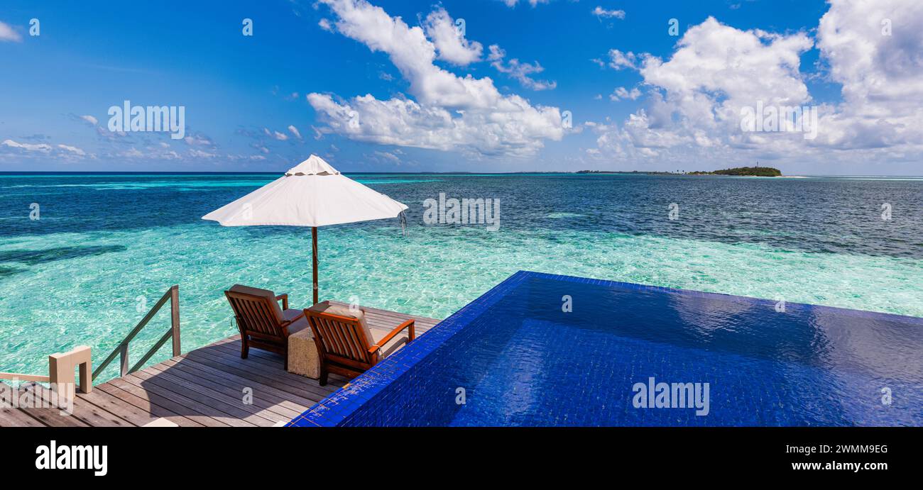 Luxury beach resort, bungalow near endless pool over beautiful blue sea. Amazing tropical island, summer vacation concept. Couple chairs with umbrella Stock Photo