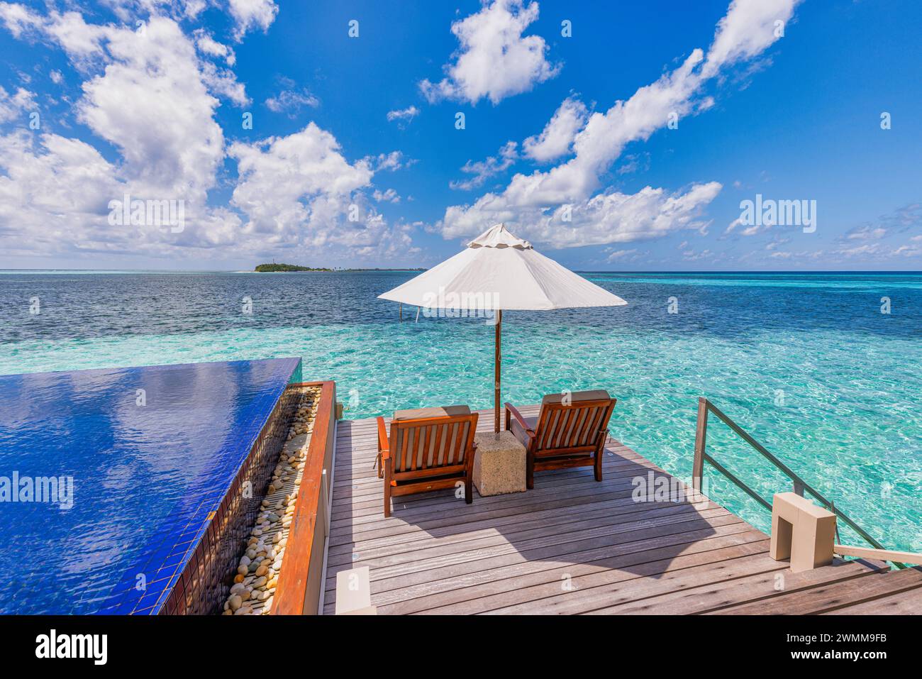 Luxury beach resort, bungalow near endless pool over beautiful blue sea. Amazing tropical island, summer vacation concept. Couple chairs with umbrella Stock Photo