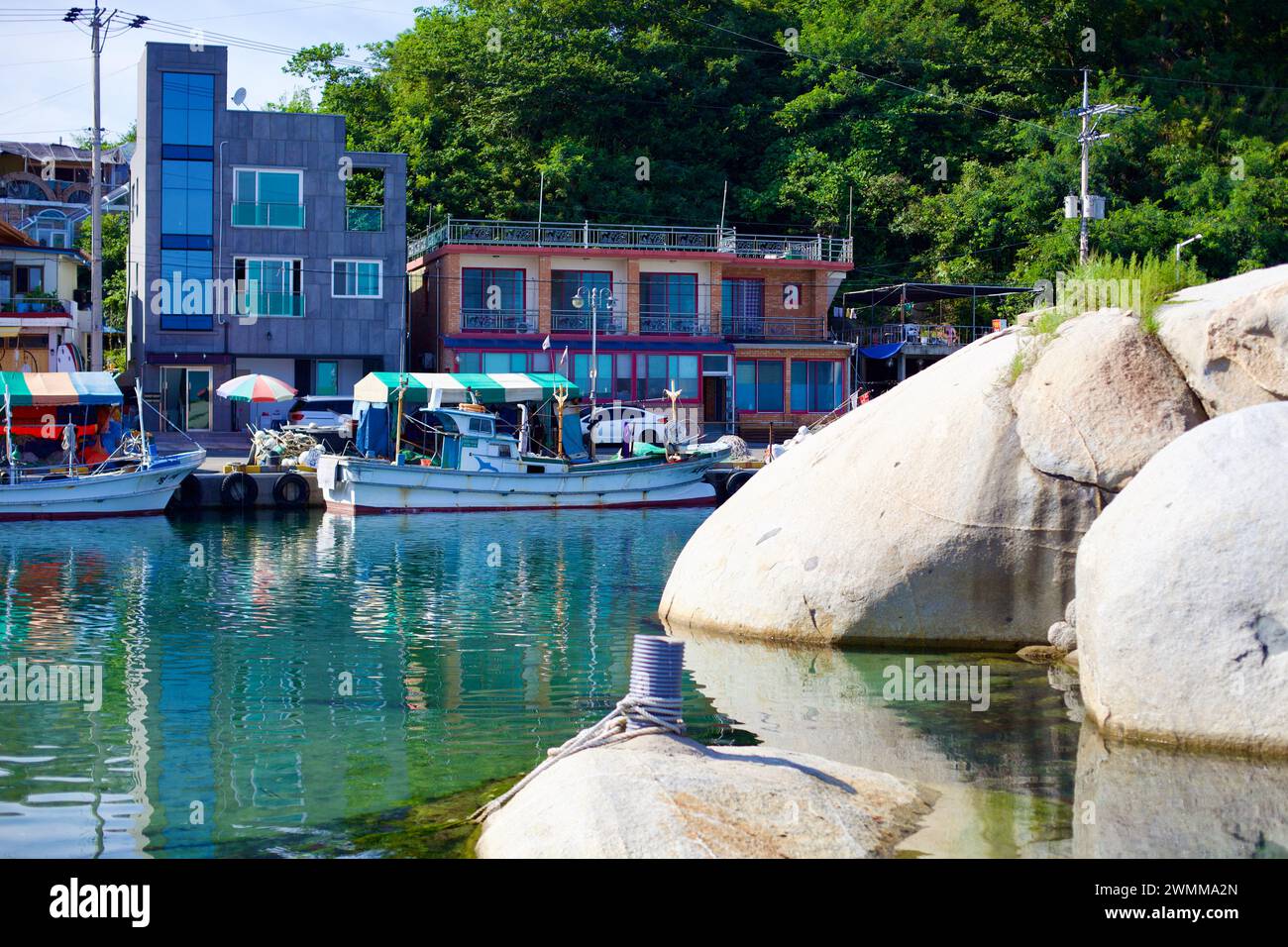 Yangyang County, South Korea - July 30th, 2019: Dongsan Port captivates with its calm waters, giant boulders, moored boats, and green hillside, reflec Stock Photo