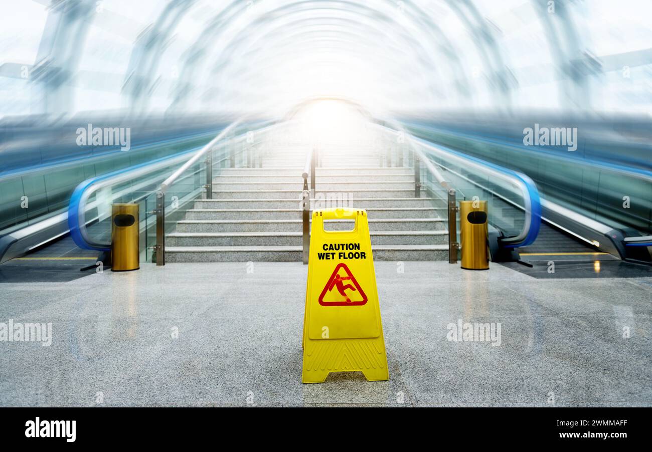 Wet floor caution sign  in front of the blurred motion escalator Stock Photo