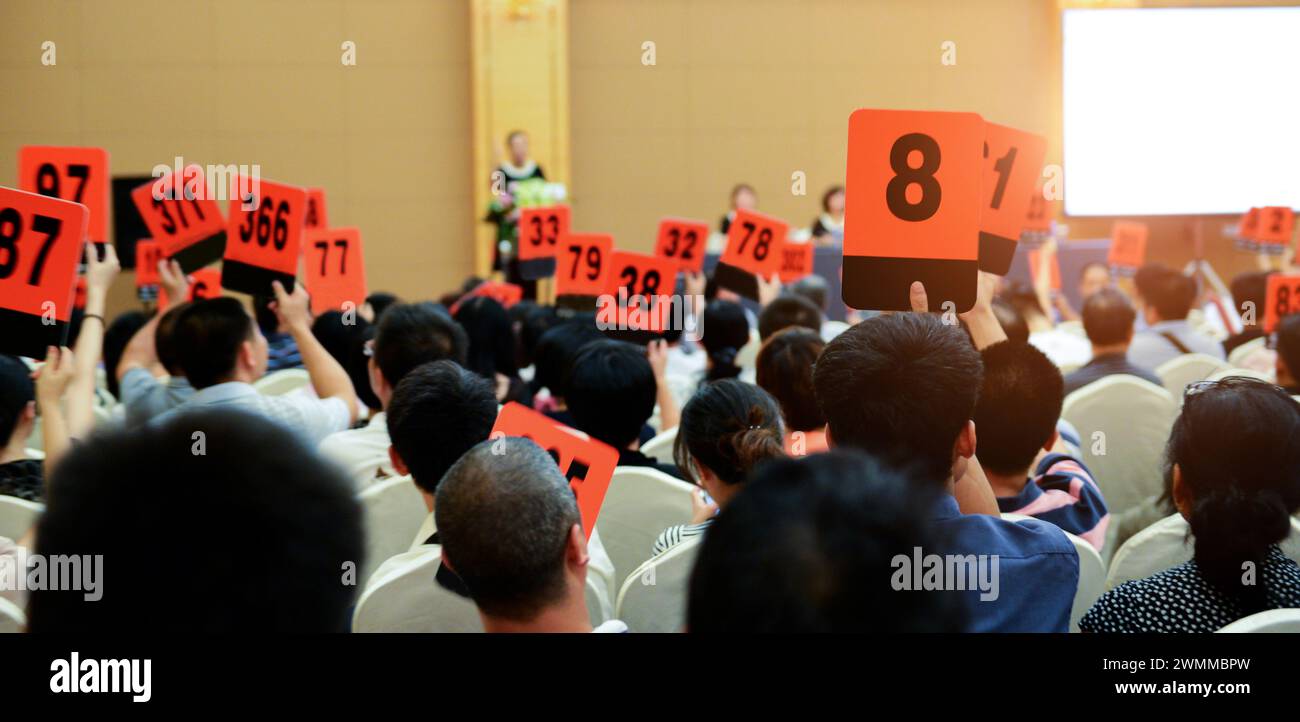 Crowd of bidders holding their numbered bidding paddles at an auction Stock Photo