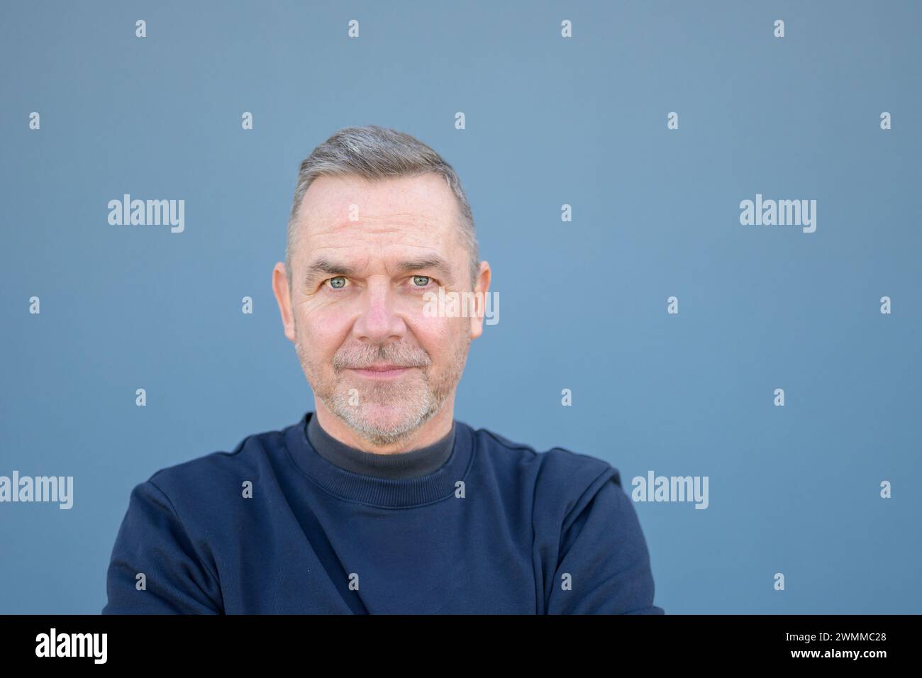 Close up portrait of a middle aged man looking doubtfully or scared at the camera with wide eyes wearing a blue sweater Stock Photo