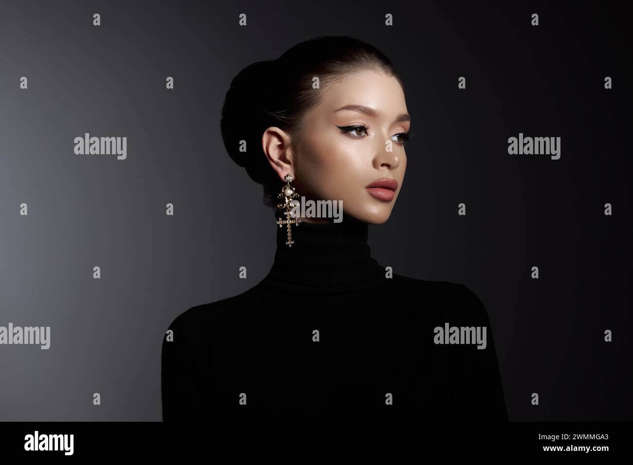Woman with elegant makeup and a cross earring poses in a black turtleneck, exuding sophistication Stock Photo