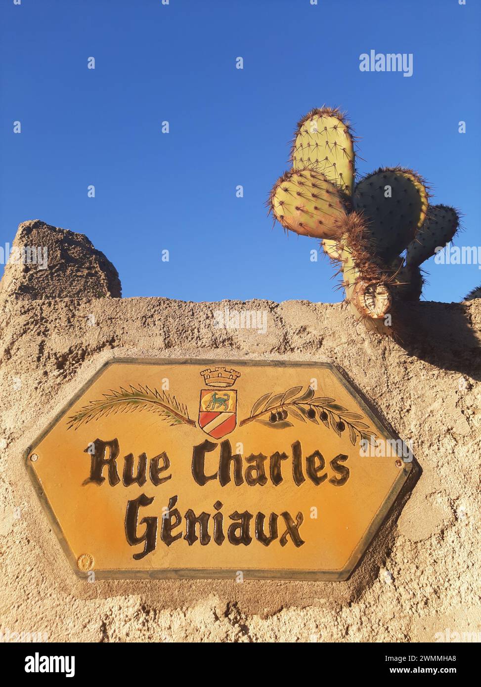 Typical porcelain ceramic street sign in Cagnes sur Mer, on a stone wall with a cactus and blue sky. Rue Charles Géniaux, 06800 Cagnes-sur-Mer, France Stock Photo