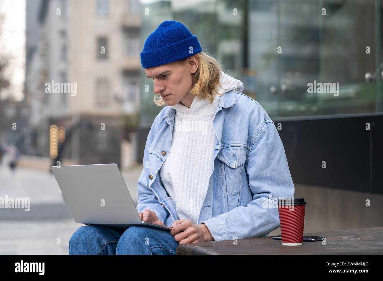 Stylish hipster guy sitting in urban street, working online, searching info in laptop computer Stock Photo