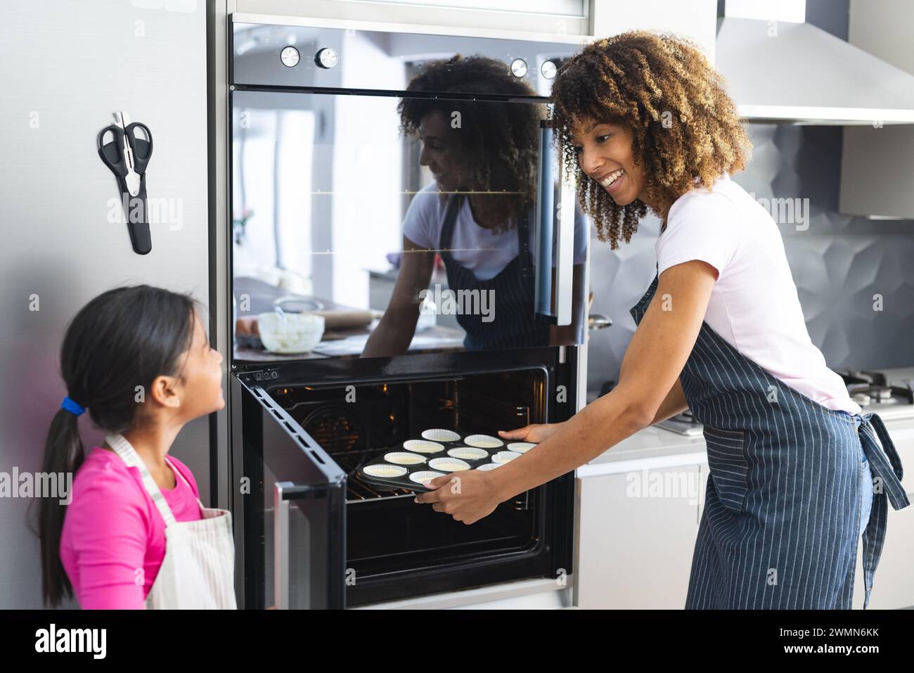 Biracial mother and daughter bake together at home for daughter in a home kitchen. They share a joyful moment preparing cupcakes, showcasing family bo Stock Photo