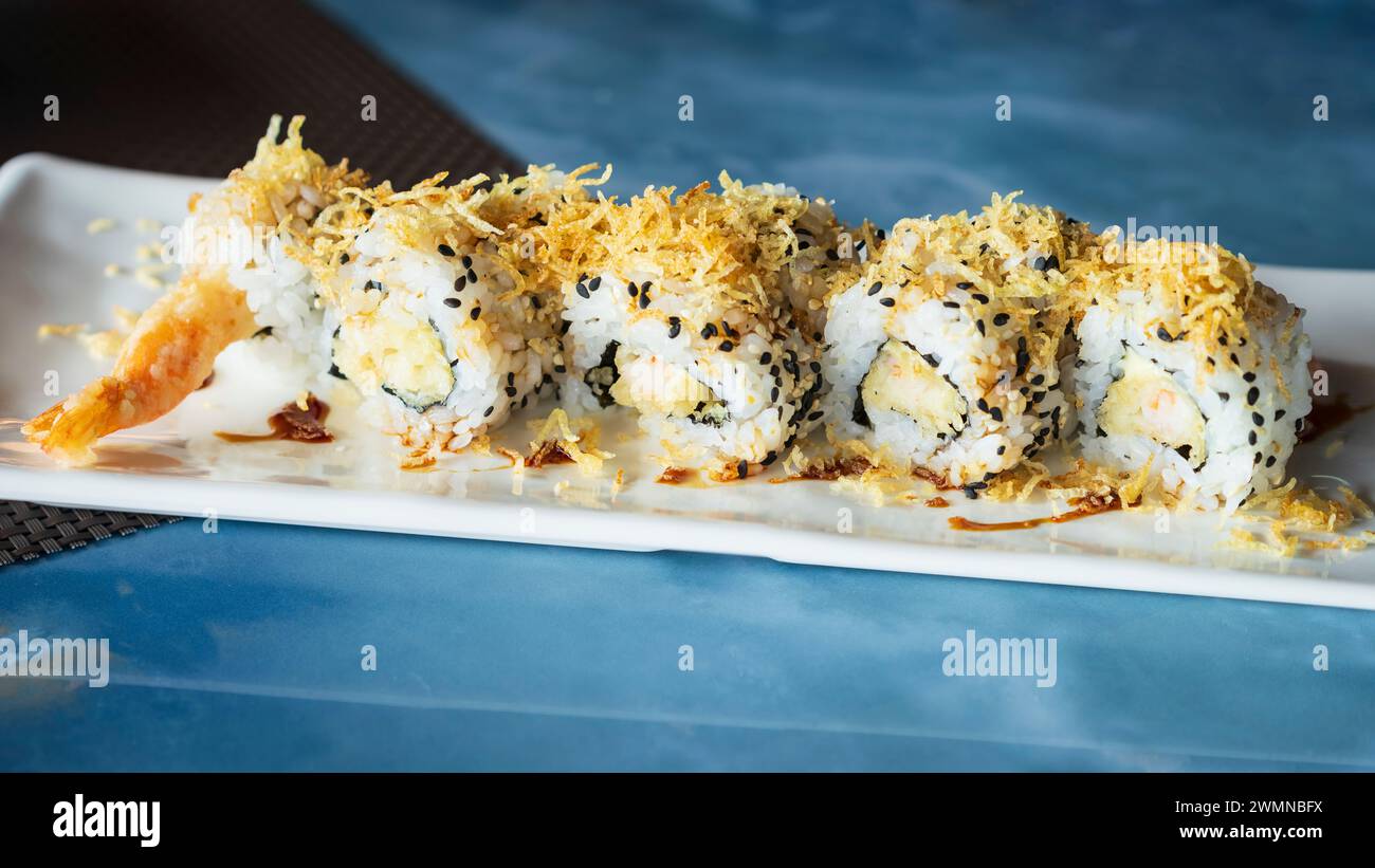 Ebi ten roll, close up view.sushi set with shrimp in tempura, oshinko, garnished with edible flower and black sesame, on an oriental tray, plate at re Stock Photo