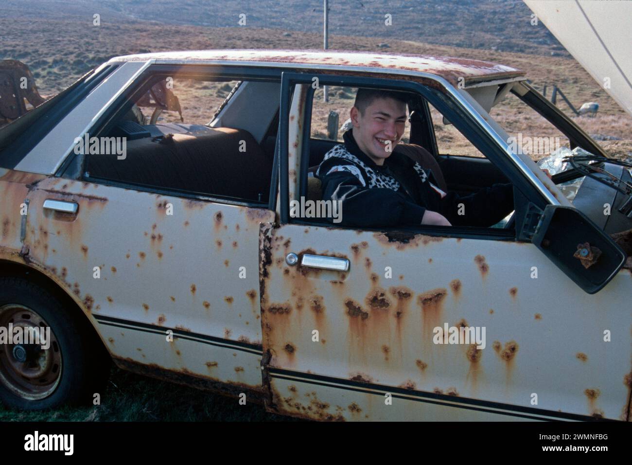 Teenager behind the wheel, Scrapped car, Dursey Island, Beara Peninsula, County Cork, Republic of Ireland, April 1996 Stock Photo