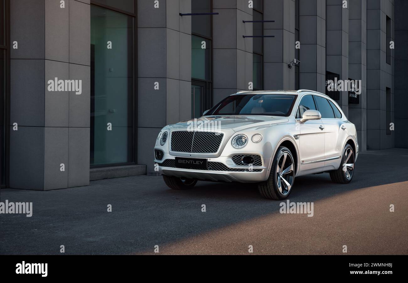 Bentley Bentayga parked near the entrance of a modern building - three quarter front view of luxury SUV at sunset near business center. Stock Photo