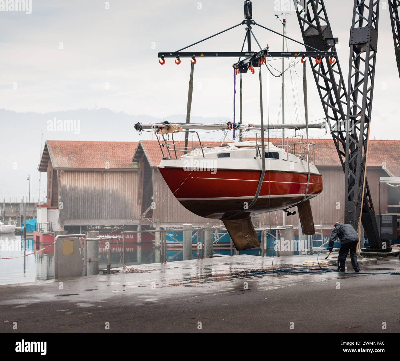 Man cleans the hull of small hanging yacht in Lindau harbor
