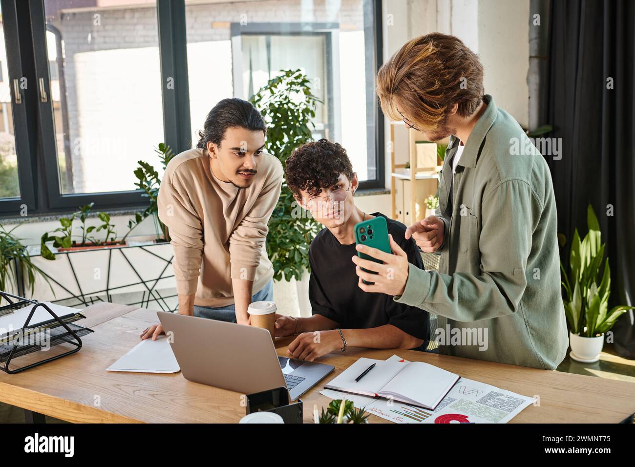 Three young professionals discussing a project and looking at smartphone while creating startup Stock Photo