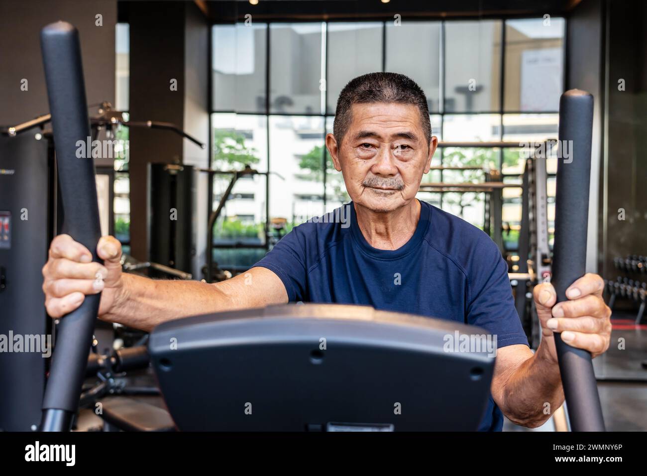 An elderly Asian male exercising on a treadmill at the gym. Stock Photo