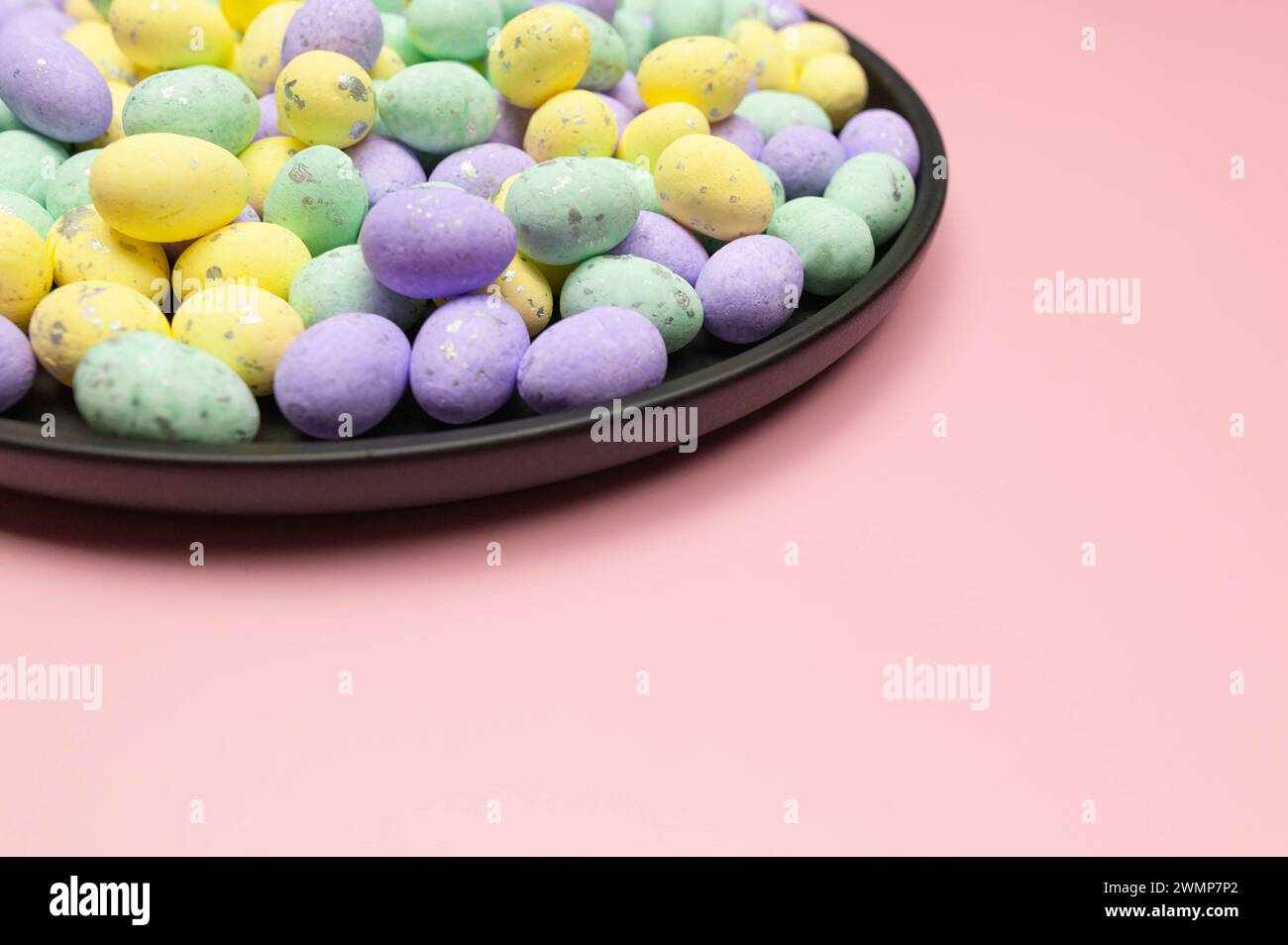Colourful easter eggs in black plate on pink background. Creative easter composition, spring, copy space. Stock Photo