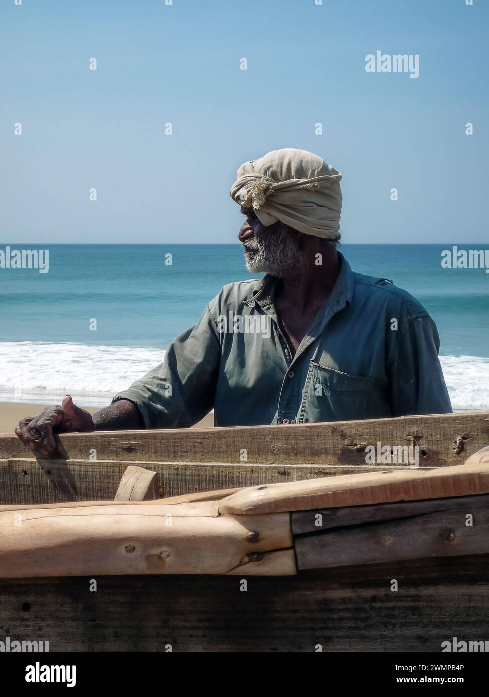 India, Kerala, Varkala: an Indian fisherman looks to his right leaning on a fishing boat on the beach of Varkala Stock Photo