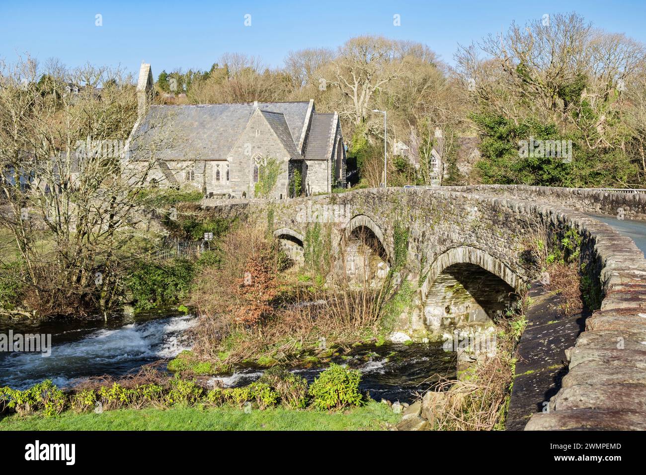 Old 18th century bridge across Afon Dwyfor River with St John's village Church beyond. Llanystumdwy, Criccieth, Llyn Peninsula, Gwynedd, north Wales Stock Photo