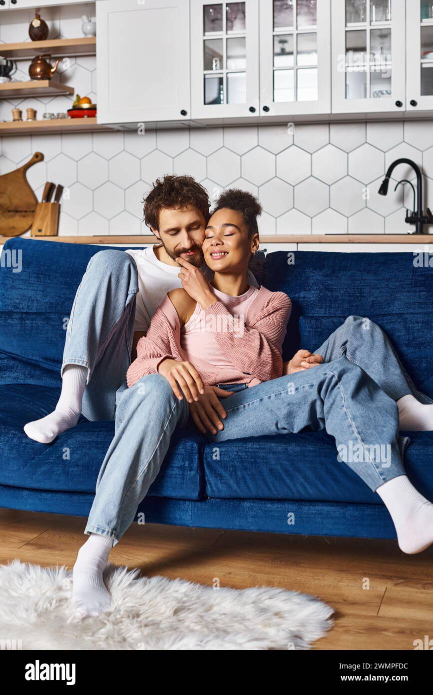 good looking contented couple in comfortable homewear hugging warmly on sofa while at home Stock Photo