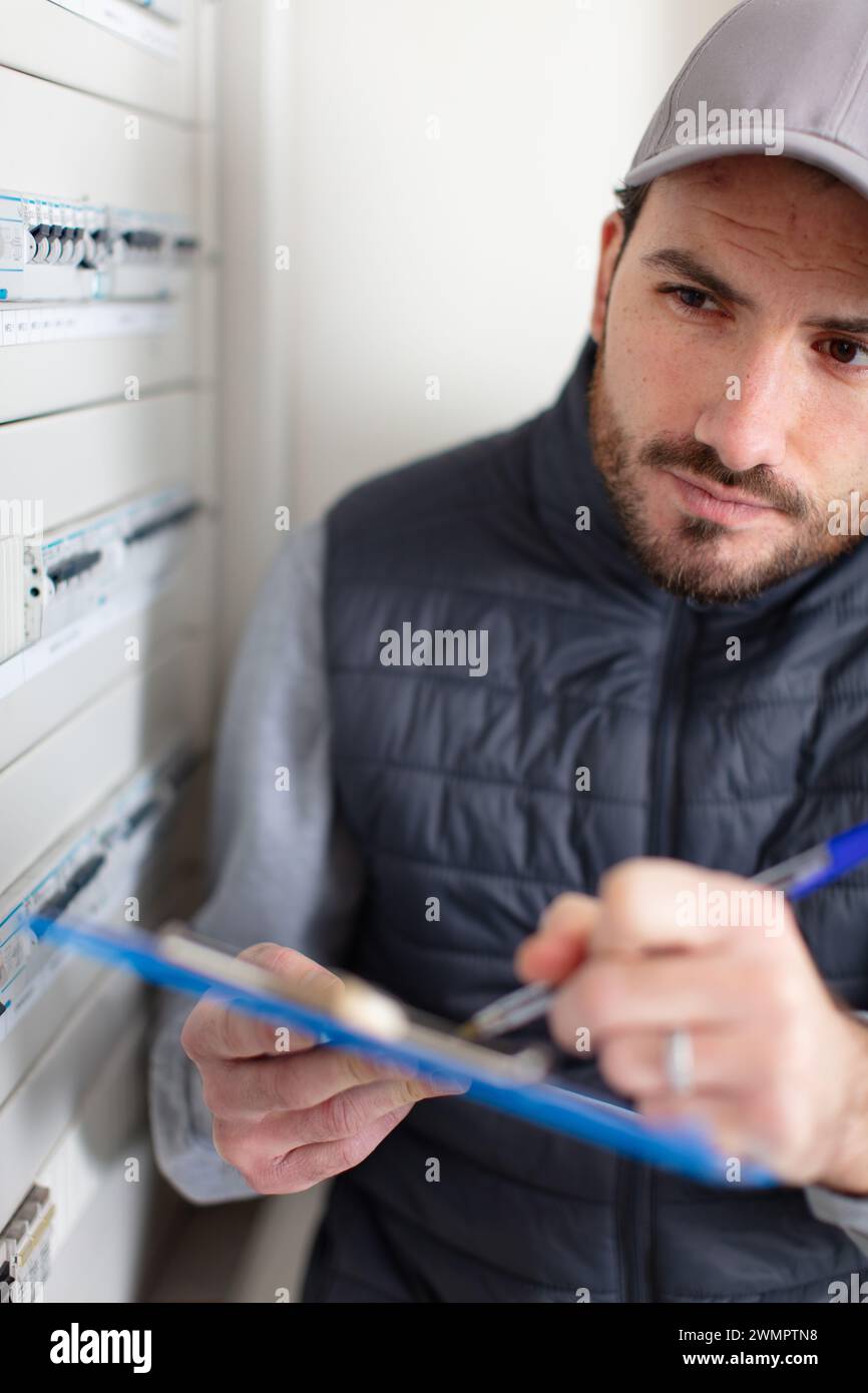 male electrician with clipboard near fuse board indoors Stock Photo